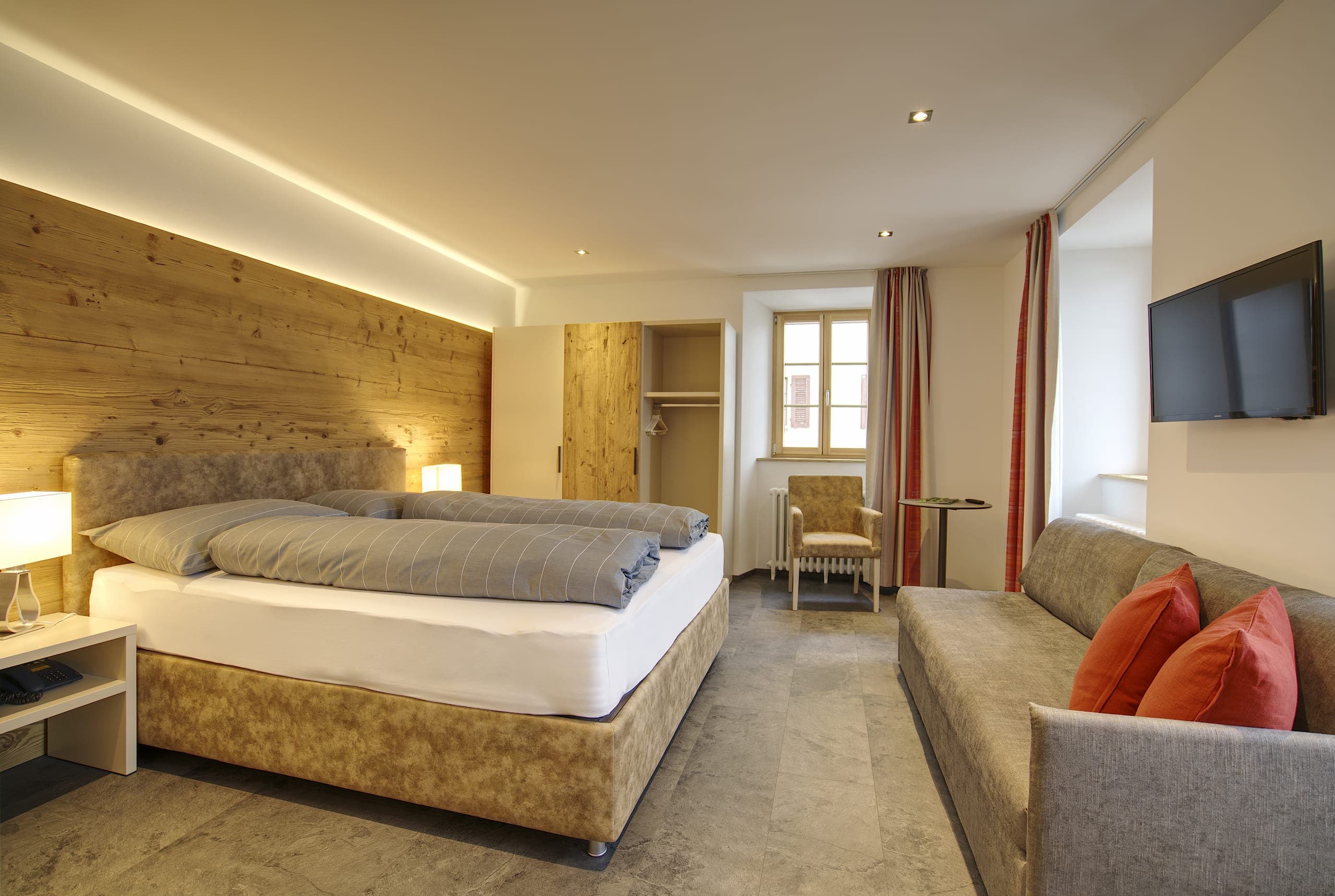 Camera doppia dell’Hotel Bellevue con parete in legno antico, divano e TV a parete.